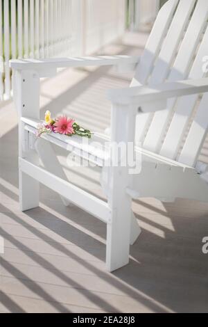 Un bouquet de fleurs couchés à la légère sur une chaise Adirondack blanche sur un porche ensoleillé. Faible profondeur de champ avec mise au point sur les fleurs. Banque D'Images