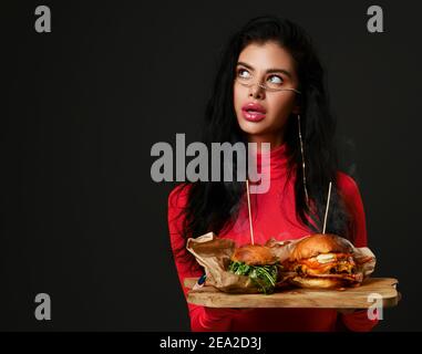 Belle femme tient deux hamburgers maison cheeseburger avec fumée chaude à la vapeur dans un chemisier rouge rose regardant le coin Banque D'Images