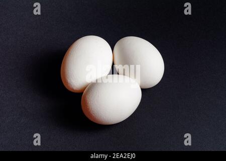 Oeufs sur fond noir, trois oeufs d'affilée, ombre sur fond d'oeufs, aliments sains et diététiques.2020 Banque D'Images