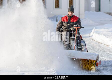 Déneigement avec brosse rotative. Homme avec une machine à balayer déneigement. Fortes précipitations et accumulation de neige. Matin d'hiver ensoleillé Banque D'Images