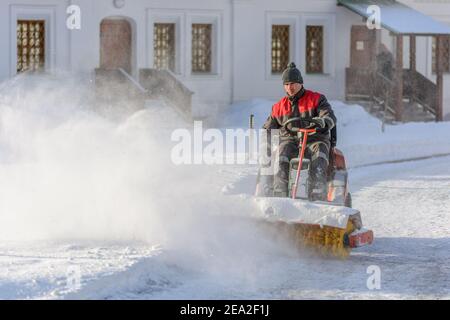 Déneigement avec brosse rotative. Homme avec une machine à balayer déneigement. Fortes précipitations et accumulation de neige. Matin d'hiver ensoleillé Banque D'Images