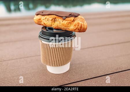 Gâteau Eclair et café chaud. Encas à emporter avec vue sur la rive de la ville dans le parc Banque D'Images