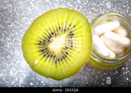 Vivace Slice de Kiwi flottant sur verre pot de pilules. Vitamine naturelle au-dessus des pilules de vitamine C. Banque D'Images