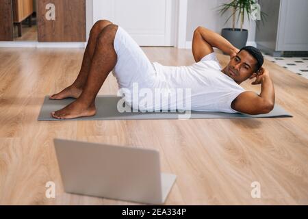 Homme afro-américain pratiquant des croquons d'abs, entraînant des muscles abdominaux sur le sol. Banque D'Images