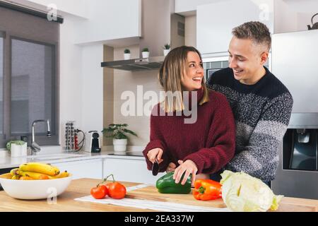 Portrait d'un jeune couple heureux en amour cuisant la nourriture végétalienne ensemble dans une cuisine moderne. Préparer un repas sain, couper des légumes Banque D'Images