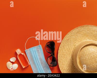 Chapeau de paille à large bord, lunettes de soleil, masque médical, désinfectant pour les mains sur fond rouge. Protection contre le covid et la grippe pendant les vacances d'été, les voyages. Banque D'Images