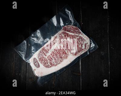 Morceau de bœuf Wagyu emballé sous vide. Steak de bœuf cru sur fond de bois dans un boucher. Produit japonais haut de gamme.