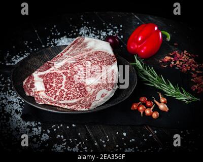 Morceau de bœuf Wagyu. Steak de bœuf cru au poivre, aux tomates et aux herbes sur fond de bois dans un boucherie de produits japonais de première qualité.