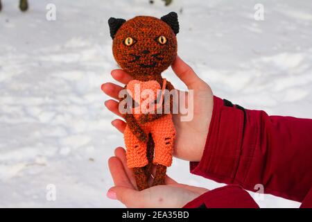 Chat jouet tricoté avec un coeur orange dans ses pattes Banque D'Images