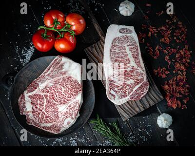 Morceaux de steak de bœuf Wagyu. Steak de bœuf cru au poivre, aux tomates et aux herbes sur fond de bois dans un boucherie de produits japonais de première qualité.