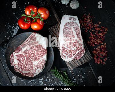 Morceaux de steak de bœuf Wagyu. Steak de bœuf cru au poivre, aux tomates et aux herbes sur fond de bois dans un boucherie de produits japonais de première qualité.