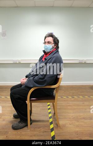 Un homme mature portant des lunettes et un masque facial s'est assis une salle d'attente de l'hôpital après avoir reçu sa vaccination contre le covid Banque D'Images