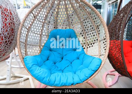 Chaise suspendue en osier, balançoire avec coussin bleu. Beau jardin moderne et tendance, mobilier de maison, canapé en rotin, siège Banque D'Images