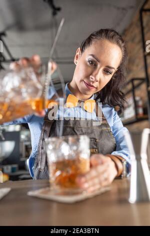 Une serveuse de bonne qualité verse un cocktail à l'ancienne dans un verre décoratif dans un pub. Banque D'Images