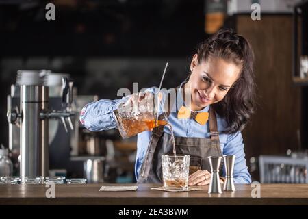 Une serveuse de bonne qualité verse un cocktail de whisky à l'ancienne dans un verre décoratif dans un pub. Banque D'Images