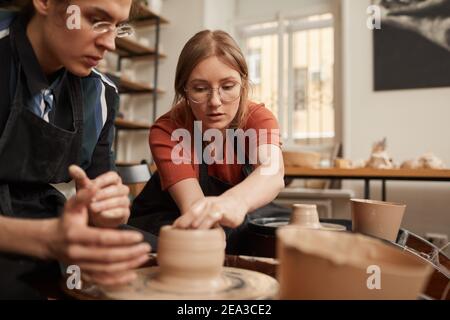 Portrait de femelle potter aidant le jeune homme à façonner l'argile sur la roue de poterie dans l'atelier, l'espace de copie Banque D'Images