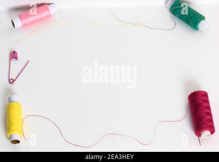 Filets dans les bobines et une broche rose sur la surface de la table blanche plane. Réparer et coudre les vêtements. Placer pour le texte. Banque D'Images