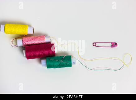 Filets dans les bobines et une broche rose sur la surface de la table blanche plane. Réparer et coudre les vêtements. Placer pour le texte. Banque D'Images