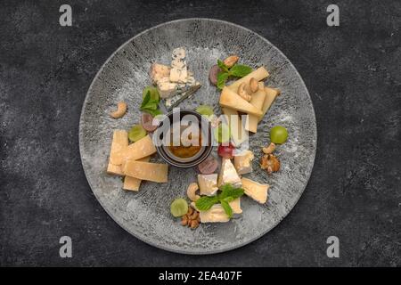 Assiette de fromages, assortiment de fromages à la menthe, fruits confits, miel et biscuits, sur une assiette, sur fond sombre Banque D'Images