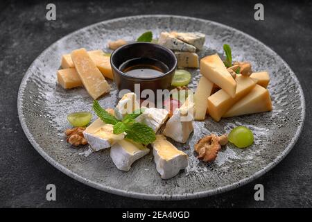 Assiette de fromages, assortiment de fromages à la menthe, fruits confits, miel et biscuits, sur une assiette, sur fond sombre Banque D'Images