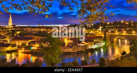 Panorama urbain de la vieille ville de Berne avec tour de la cathédrale et pont Nydeggbr cke illuminé la nuit et reflétant la rivière Aare. Site populaire Banque D'Images