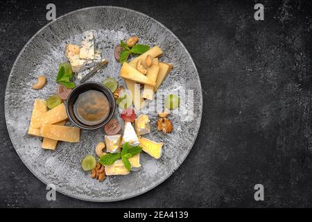 Assiette de fromages, assortiment de fromages à la menthe, fruits confits, miel et biscuits, sur une assiette, sur fond sombre Banque D'Images