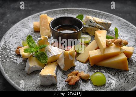 Assiette de fromages, assortiment de fromages à la menthe, fruits confits, miel et biscuits, sur une assiette, sur fond sombre Banque D'Images