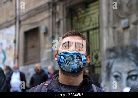 Un jeune fan de Naples avec masque, peint avec des images de Maradona, regarde les images de la Pibe de Oro , dans les quartiers espagnols. Banque D'Images