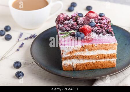 Gâteau aux baies avec crème au lait et confiture de myrtilles sur une assiette en céramique bleue avec une tasse de café et des myrtilles fraîches sur fond de bois blanc. Vue latérale, c Banque D'Images