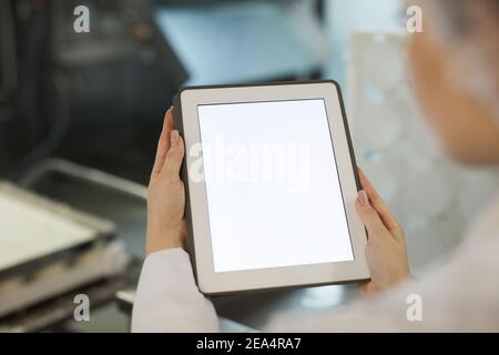 Gros plan d'une employée tenant une tablette numérique avec écran blanc vierge contre l'équipement de l'usine en arrière-plan, espace de copie Banque D'Images