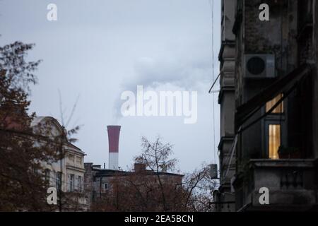 Cheminée rouge industrielle d'une usine qui travaille et libère des fumées et des fumées toxiques dans l'atmosphère entourée de bâtiments résidentiels à Belgrade, SER Banque D'Images