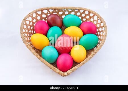 Oeufs de pâques colorés peints dans un panier brun. Un panier en paille sous forme de coeur avec des oeufs colorés peints pour le Saint chrétien orthodoxe Banque D'Images