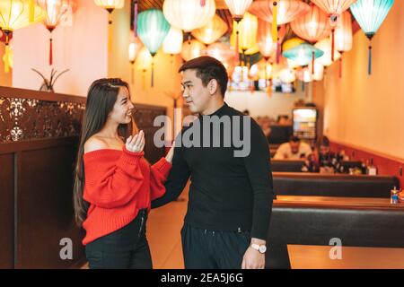 Beau jeune couple asiatique en vêtements rouges donner présent dedans restaurant chinois vietnamien festif lanternes en papier colorées Banque D'Images