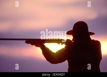 Silhouette de chasseur tirant un fusil au coucher du soleil Banque D'Images