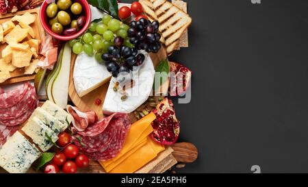 Table de hors-d'œuvre. Fromage, fuits et carton de viande sur fond sombre. Vue de dessus, espace de copie Banque D'Images