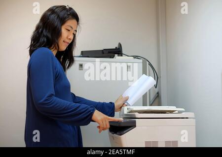 Une femme asiatique d'âge moyen, travaillant comme secrétaire, copie des documents à l'aide d'une imprimante laser multifonction à son bureau. Banque D'Images