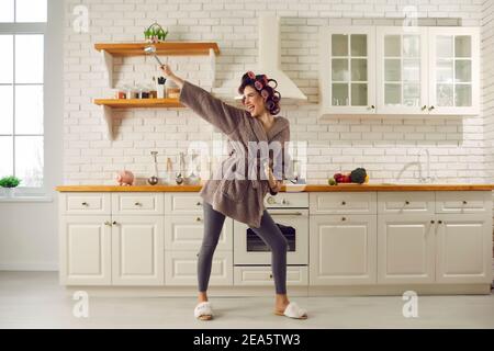 Bonne jeune femme chantant et dansant tout en cuisinant le petit déjeuner cuisine spacieuse Banque D'Images
