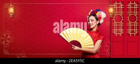 Belle femme asiatique souriante portant une robe traditionnelle avec un ventilateur doré et couronne de fleurs sur la tête en bannière rouge de style oriental arrière-plan avec copie sp Banque D'Images