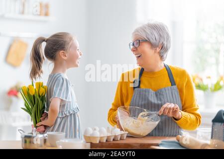 Une famille heureuse et aimante prépare la boulangerie ensemble. La petite fille donne des fleurs à sa granny dans la cuisine. Banque D'Images