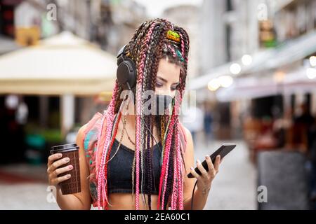 Ludique cool Rebel Funky hippster jeune fille avec masque de visage recherche de la musique de la liste de lecture sur le téléphone mobile pendant que vous marchez rue de la ville Banque D'Images