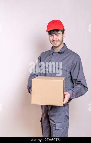 Liveur avec boîte en carton dans ses mains livrant la commande, vêtu d'uniforme et souriant, avec capuchon rouge Banque D'Images