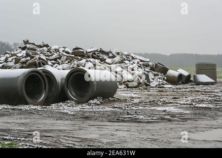 Tuyaux en béton cassés et neufs pour l'installation de drainage sur un chantier de construction dans le champ par une journée humide et enneigée, concentration sélectionnée, profondeur de fi étroite Banque D'Images