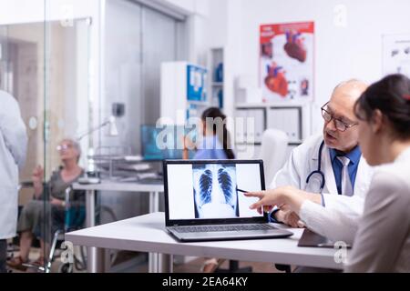 Radiologue examinant les rayons X numériques de la femme pendant les consultations, expliquant le traitement en consultation à l'hôpital. Médecin senior montrant le pointage des résultats de radiographie avec un pochoir sur le bureau d'un ordinateur portable Banque D'Images