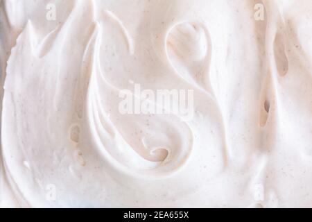 Texture crémeuse de mousse blanche aérée à gommage aux particules. Arrière-plan cosmétique avec lumière chaude et teinte de bec Banque D'Images