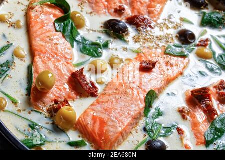 Plat de saumon toscan de filet de saumon poêlé à la peau avec sauce à la crème, ail, poireaux, tomates séchées, olives et épinards sur un plat de cuisson noir Banque D'Images