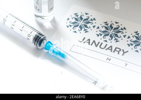 Gros plan d'une seringue médicale placée sur un calendrier de janvier avec un flacon de vaccin en arrière-plan, symbolisant la vaccination programmée Banque D'Images