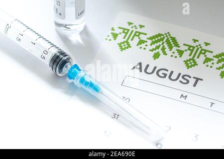 Gros plan d'une seringue médicale placée sur un calendrier d'août avec un flacon de vaccin en arrière-plan, symbolisant la vaccination programmée Banque D'Images