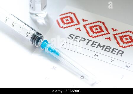 Gros plan d’une seringue médicale placée sur un calendrier de septembre avec un flacon de vaccin en arrière-plan, symbolisant la vaccination programmée Banque D'Images