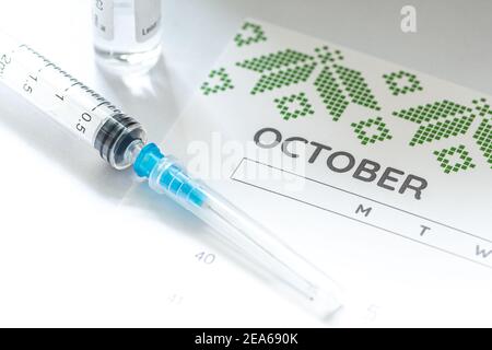 Gros plan d'une seringue médicale placée sur un calendrier d'octobre avec un flacon de vaccin en arrière-plan, symbolisant la vaccination programmée Banque D'Images