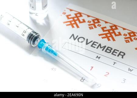 Gros plan d’une seringue médicale placée sur un calendrier de novembre avec un flacon de vaccin en arrière-plan, symbolisant la vaccination programmée Banque D'Images